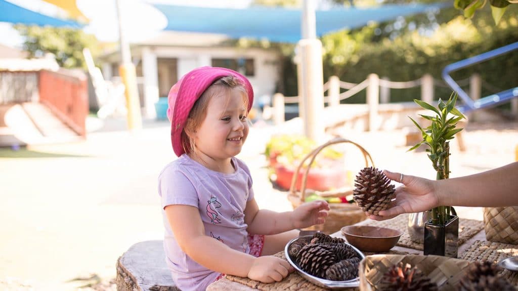 a child being offered a pine cone from a teacher