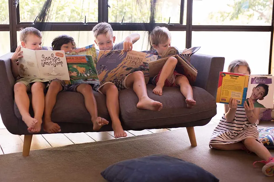 A few kids are sitting beside each other reading some books.